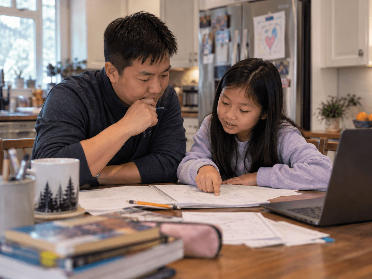 A student explaining her written work to a parent at the kitchen table.