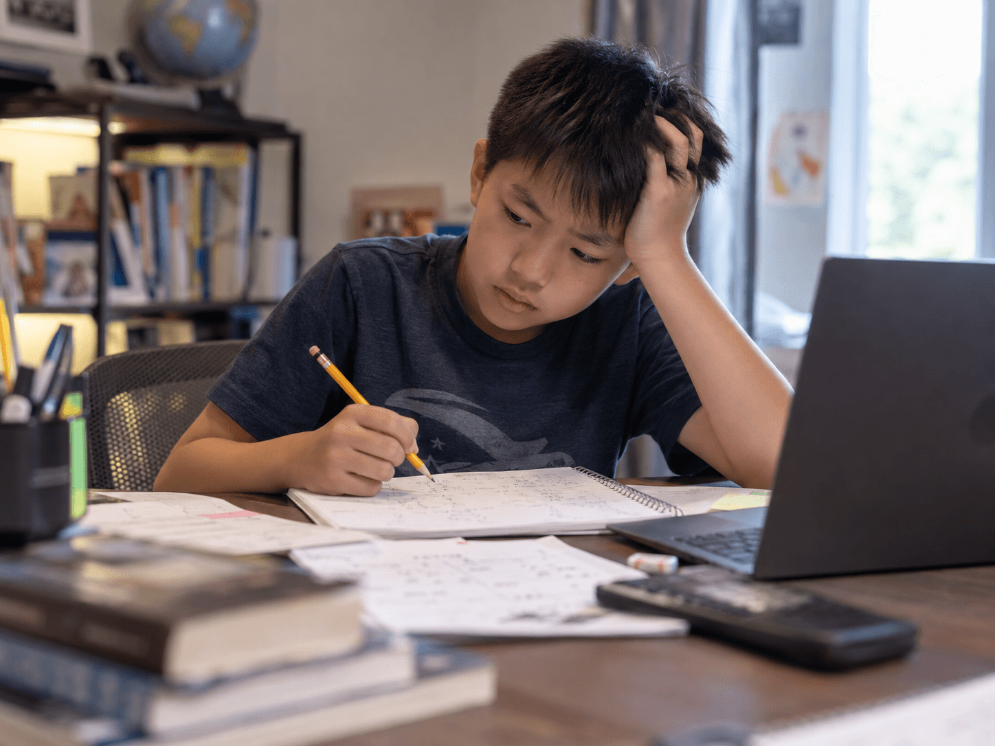 A student pausing with a pencil over his notebook, one hand in his hair.