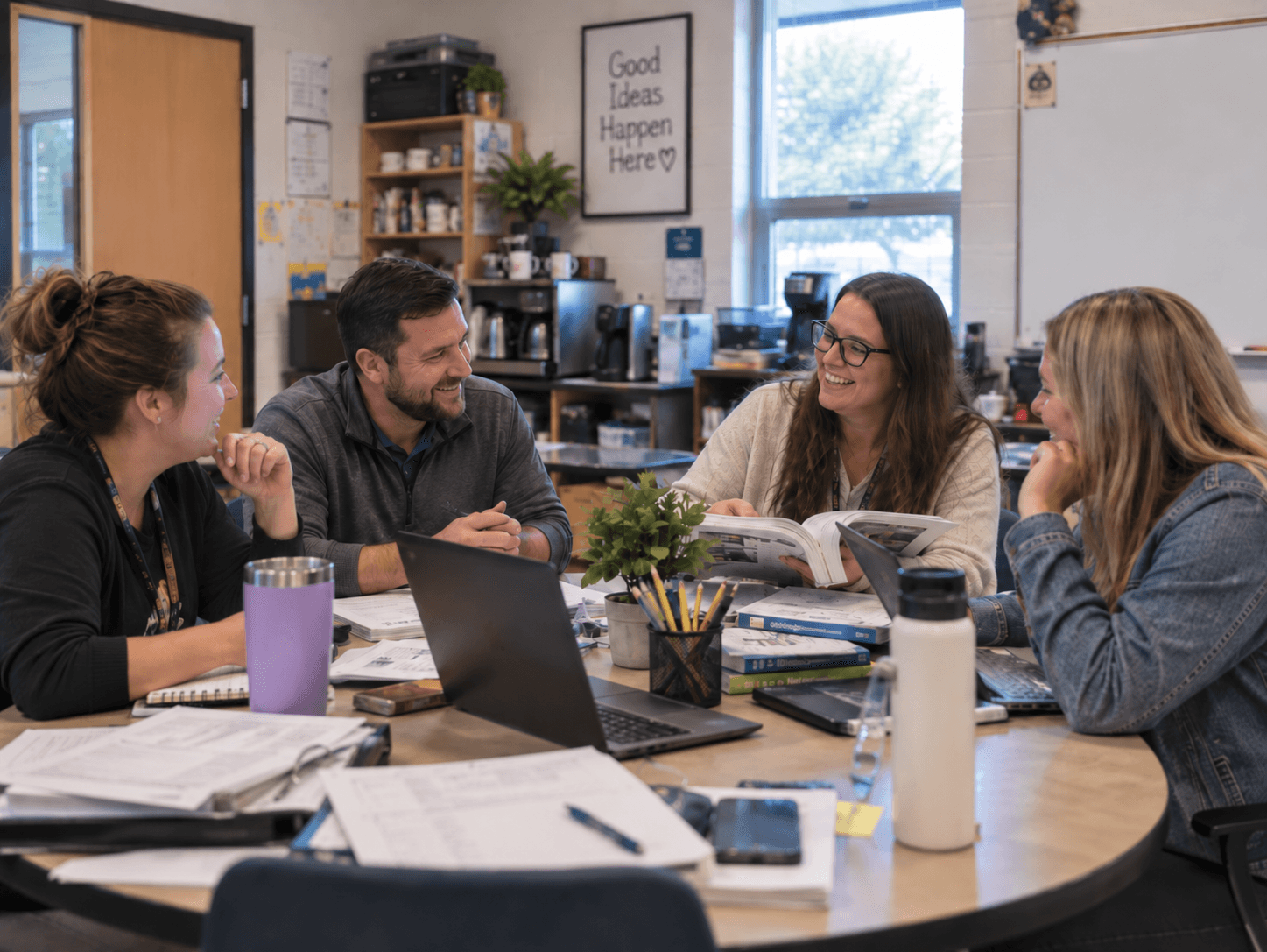 Four teachers sharing ideas around a table with notebooks and a laptop.